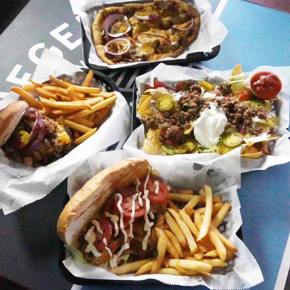 Table setting featuring Empire Street Burger with Fries, BBQ Pork Flatbread, Stadium Nachos, and Blackened Whitefish Po’ Boy